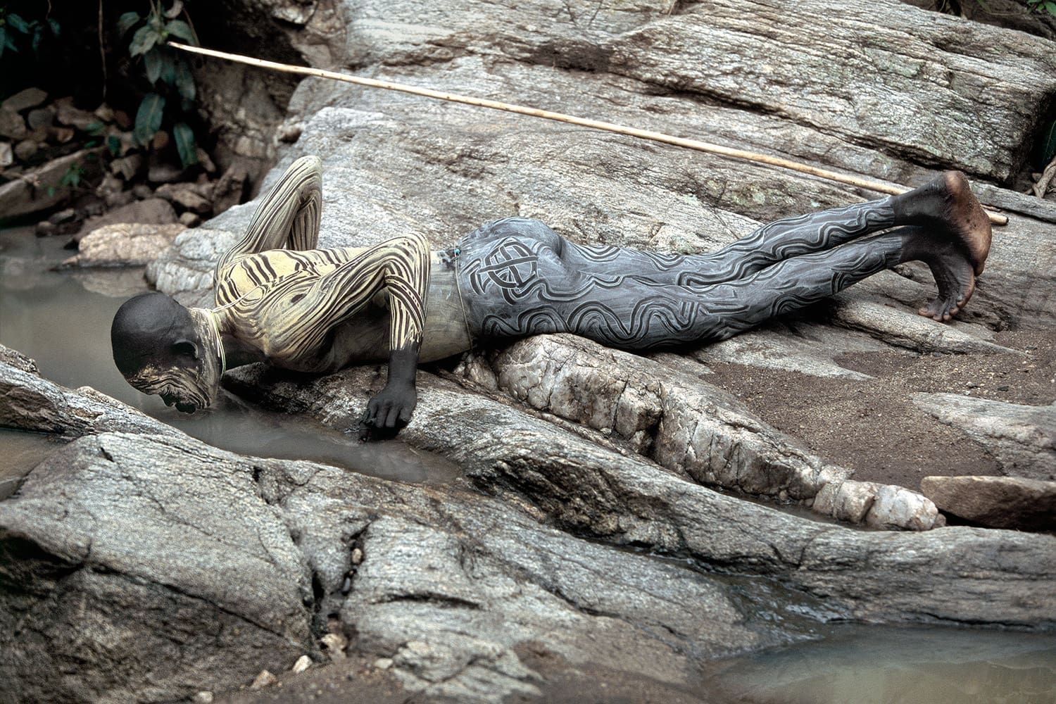 Photograph of a warrior from the omo valley drinking in a stream.